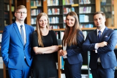 Czterech słuchaczy (dwie panie w środku i dwóch panów) stoją w bibliotece na tle regałów z książkami