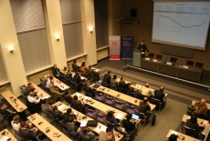 Widok na aulę i siedzących uczestników  przy mównicy przemawia Pan